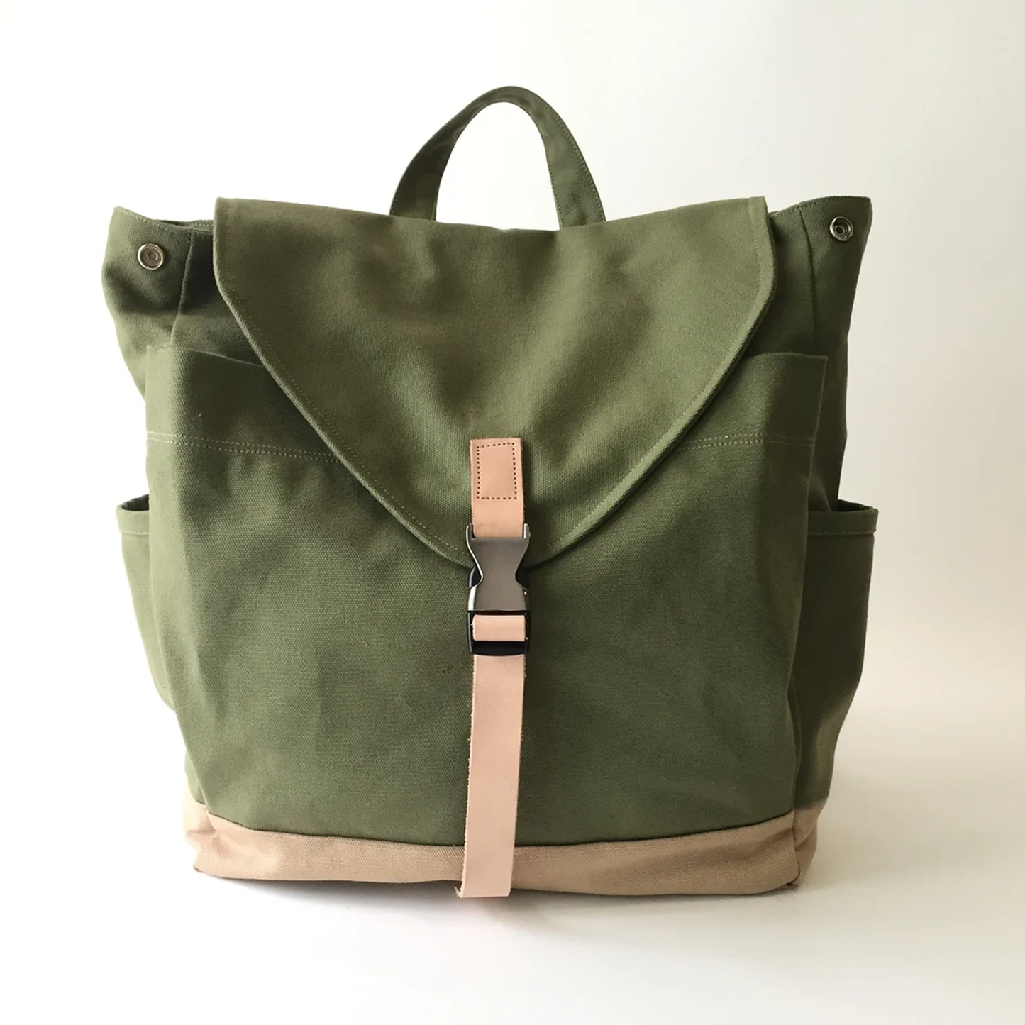 Moss Green And Beige Two-Tone Flap Backpack With Pale Pink Buckle Strap, Dual Side Slip Pockets And Rounded Fabric Top Carry Loop